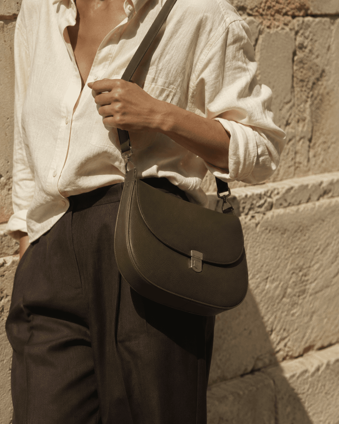 Olive leather shoulder bag styled with ivory linen in warm sunlight
